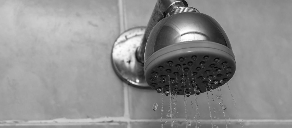 A closeup grayscale shot of a showerhead with water dripping down