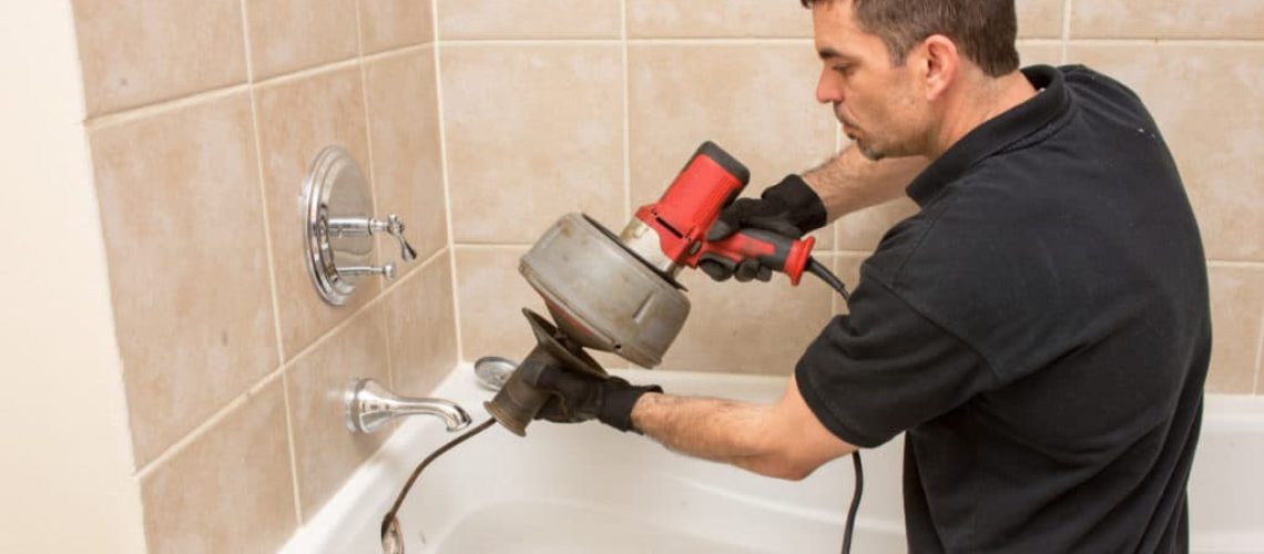 Man using a drain snake on his clogged bathtub sink during a plumbing emergency