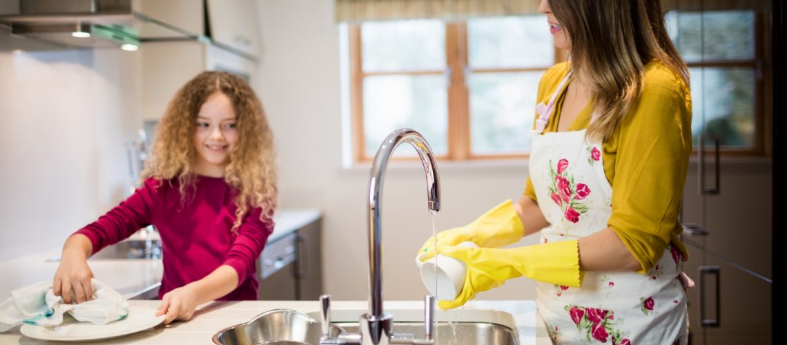 Mother and daughter washing dishes in kitchen, making sure to prevent clogged or blocked sink