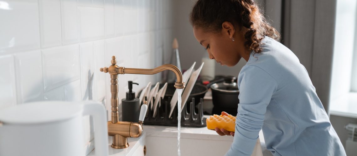 Young woman doing dishes at her kitchen sink, making sure not to pour anything down the drain that may clog it.